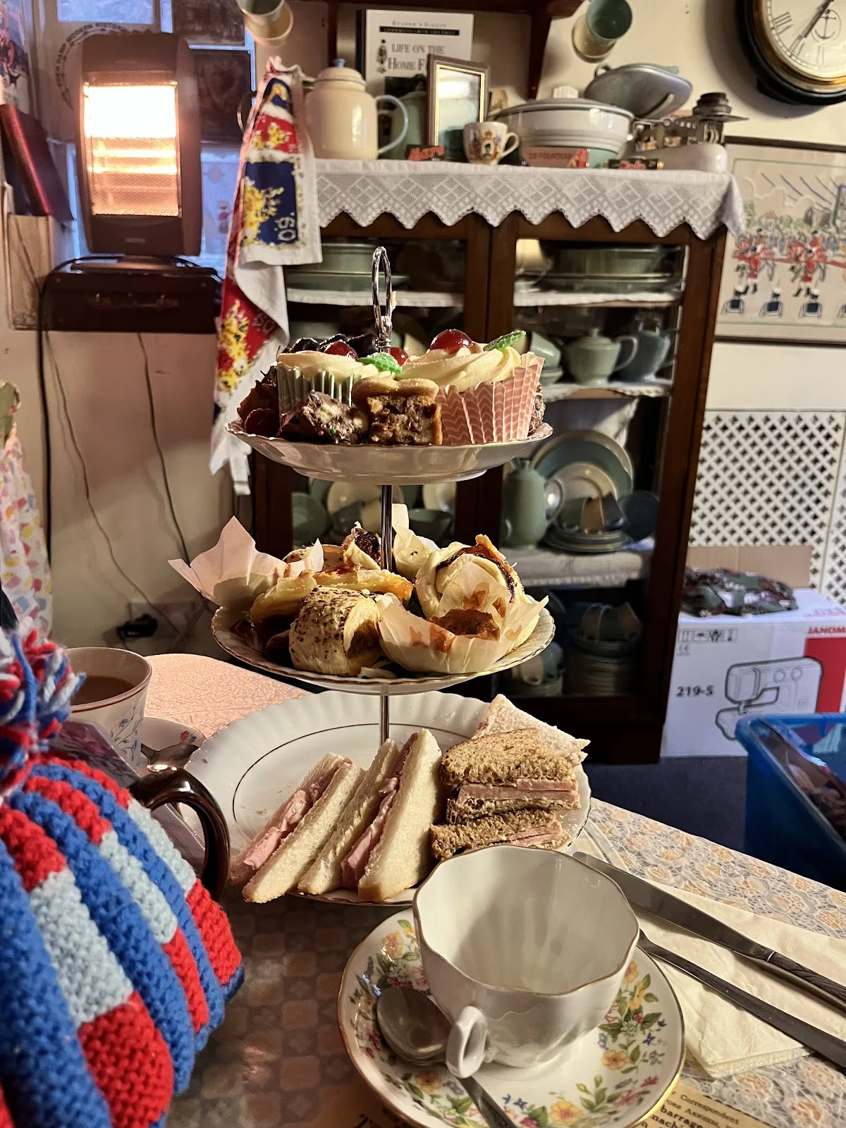A three tier afternoon tea stand at 19 Fourteas with finger sandwiches, savoury pastries and cakes, beside a floral teacup